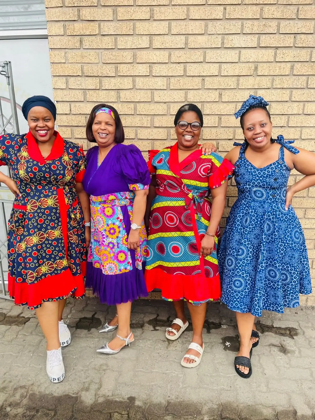Four women in vibrant patterned dresses posing together