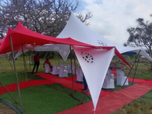 Red-and-white stretch tents with red carpet at an outdoor service