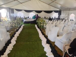 Decorated white funeral tent with chairs, floral aisle and green carpet
