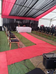 Funeral tent with red-and-black draping, red carpet, chairs and a stage