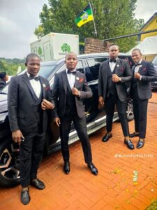 Formally dressed pallbearers standing beside a black vehicle