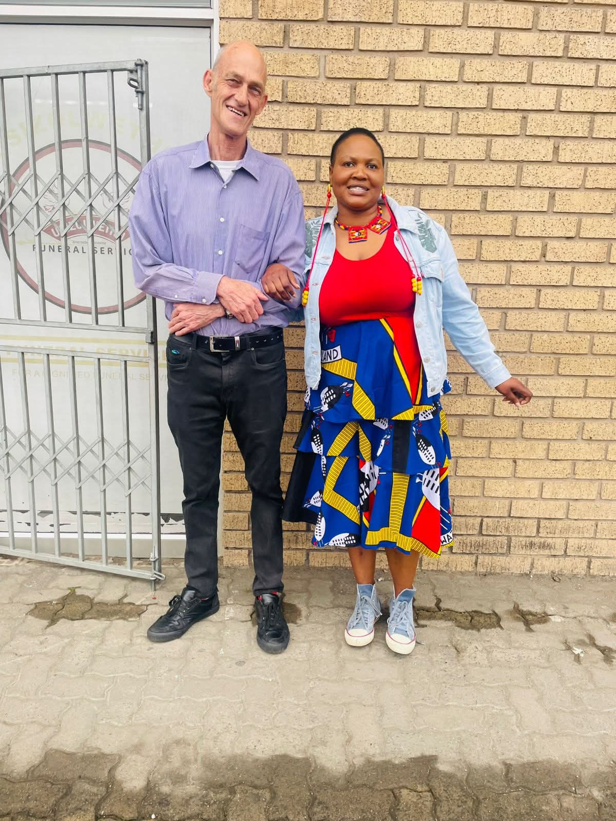 Two people posing together in front of a brick wall